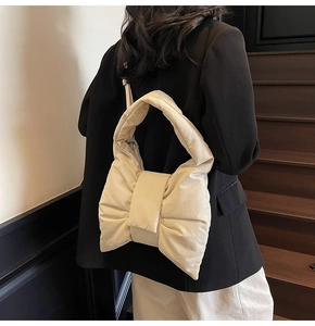 Detail of a cream large bow shoulder bag with elegant fabric folds on a model