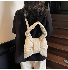 Detail of cream white bow-shaped quilted shoulder bag worn by model on stairs