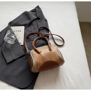 Detail of color-block bowling handbag with brown leather and blue piping on white fabric