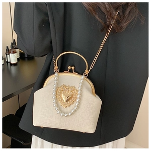 Detail of cream white shell bag with pearl trim and gold heart emblem on black suit