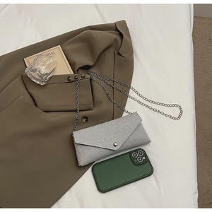 Silver glitter envelope chain bag shown on white fabric with fashion accessories