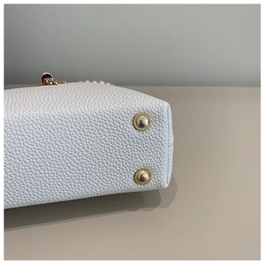 Detail of white lychee leather texture with protective gold metal feet on shell bag