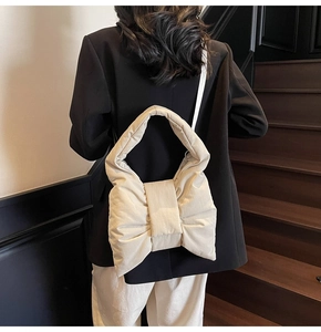 Close-up of beige quilted nylon handbag featuring a large fashion bow and slim strap