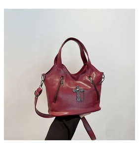 Macro detail of wine red tote bag with gothic cross pendant and metal chain accents
