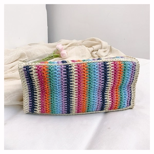 Detailed view of the multi-color rainbow woven straw bag on a white textured fabric