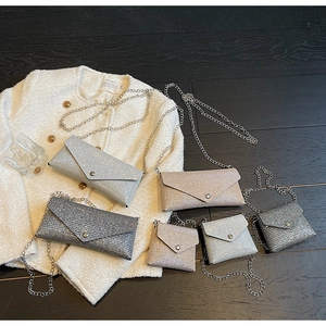 Macro shot of glittery envelope chain bags in silver and gold on a wood floor