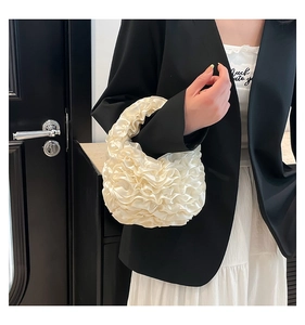 Detail of cream white pleated satin handbag held by model in elegant monochrome setting