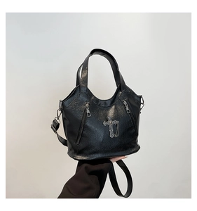 Close-up of black litchi grain leather tote featuring metallic cross pendant and zippers