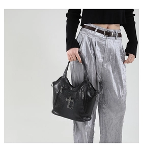 Detail of black pebbled leather tote bag with punk cross and metal chain decoration