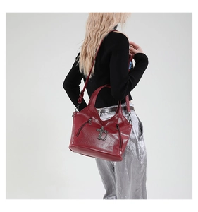 Side view of woman carrying a burgundy punk tote bag with metal cross and zipper detail
