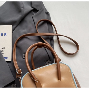 Macro detail of camel brown leather bowling bag with blue piping and round handle