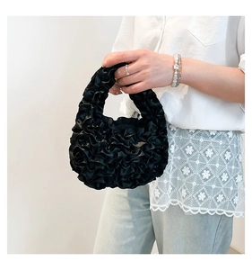 Detail of black pleated lace handbag with ruffled satin fabric and integrated handle design