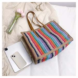 Flat lay of colorful striped straw tote bag with brown leather handles and pink tulips