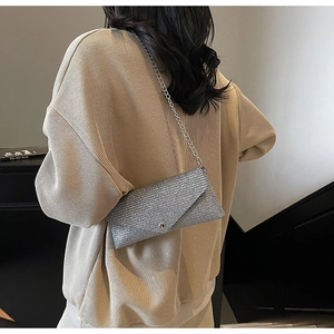 Silver sequin envelope bag with metal chain strap worn on a beige ribbed sweater