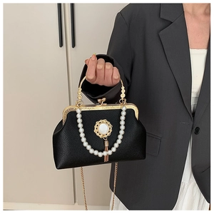 Close-up of black leather bag with baroque pearl chain, gold handle and metal tassels