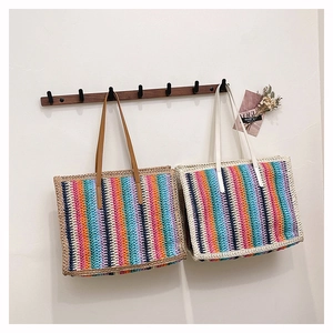 Detail of handmade rainbow striped straw tote bag featuring brown leather handle and texture