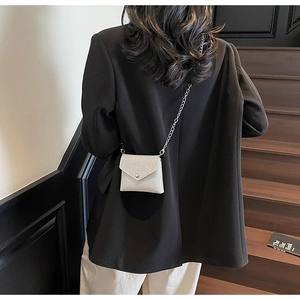 Detail of silver sequin mini envelope crossbody bag with metal chain on black blazer