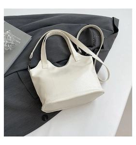Detail of white lychee grain leather tote bag with punk cross accents on grey suit background