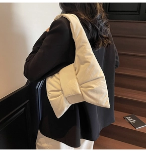 Close-up of cream white bow-shaped puffy nylon tote bag on a wooden staircase