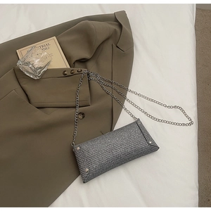Detail of silver sequin crossbody bag with chain strap on a stylish blazer background