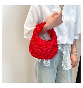 Detailed view of red ruffled pleated handbag in silk-like finish held by a model