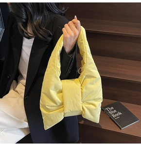 Close-up of bright yellow bow-shaped nylon handbag held by a model on wooden stairs