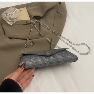 Detail of silver glitter envelope clutch bag with thin metal chain strap on beige blazer
