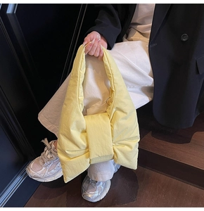 Detail of soft yellow nylon tote bag featuring a large decorative bow and padded texture