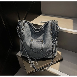 Close-up of washed denim tote with metal studs and leather chain straps on a book