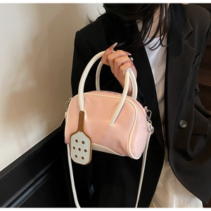 Pink and white shoulder bag with decorative pendant worn over a black blazer