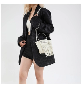 Close-up of white shell bag with metallic rivets and long fringe tassels on model