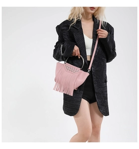 Detail of pink tassel crossbody bag with metallic silver studs and round handle worn by model