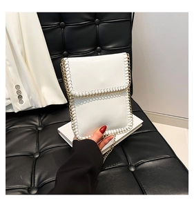 Close-up of white minimalist phone bag with gold chain edge and matching metal strap