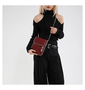 Detailed view of dark red glossy shoulder bag with silver chain trim on a black outfit