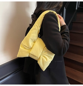 Detail of a bright yellow nylon puffer shoulder bag with a unique oversized bow design