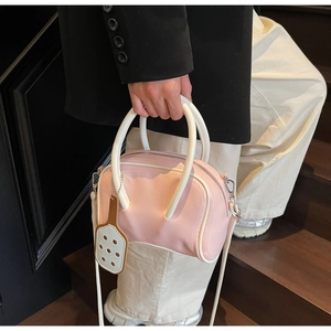 Pink shoulder bag with white handles and charm accessory held by a model on stairs