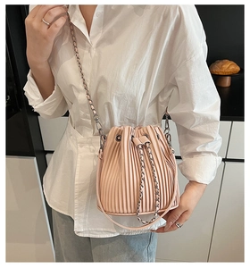Detail of light pink bucket bag with pleated texture and silver metal chain strap