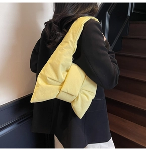 Pale yellow quilted nylon tote bag with large bow design worn by a model on stairs