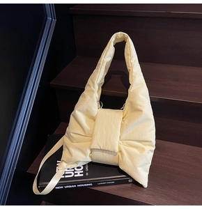 Close-up of pale yellow quilted puffer tote bag with bow design on wooden stairs