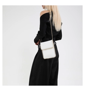 Mini white crossbody bag with gold chain edge detail shown on model in black outfit