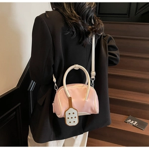 Detail of pink and white Boston bag with racket charm carried by model in black suit