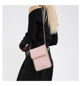 Detail view of pink glossy crossbody phone bag with gold chain strap on black outfit
