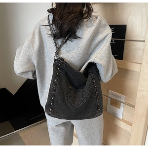 Detail of dark wash denim tote bag with metal studs and chain strap on female model