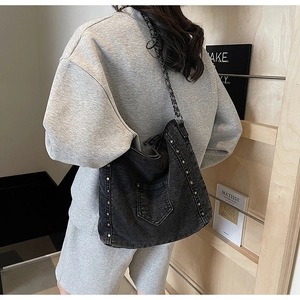 Detail of dark grey washed denim messenger bag with silver rivets and metal chain strap