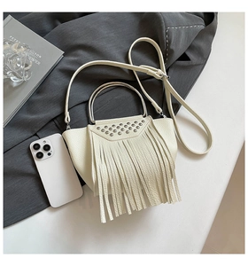 Detail of cream shell bag with leather tassels, metallic studs, and silver ring handle