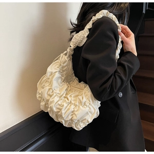 Side view of cream pleated dumpling bag on shoulder showing its puff texture and size