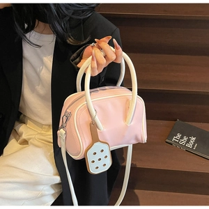 Detail of pink macaron Boston bag with cream straps shown on a model in dark blazer