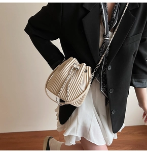 Detailed view of cream pleated bucket bag with chain strap styled on a fashion model