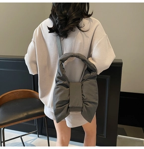 Detail of dark gray oversized bow-knot nylon shoulder bag on a model in a modern interior