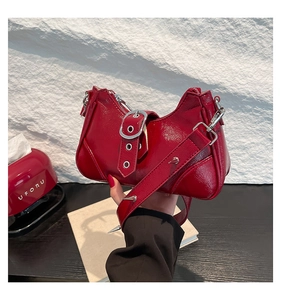 Détail du sac bandoulière en cuir verni rouge avec boucle argentée et clous décoratifs